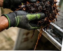 Gloved hands removing leaves and debris from a gutter